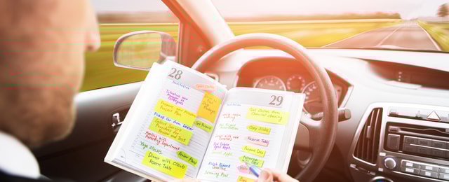 Autofahrer führt ein Fahrtenbuch per Stift am Steuer.